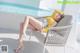 A woman in a yellow sweater is sitting on a chair by the pool.