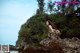 A woman sitting on top of a rock near the ocean.