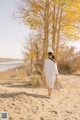 A woman walking on a sandy beach next to a tree.