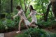 Two naked women walking through a lush green forest.