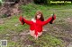 A woman in a red bodysuit and high heels sitting on the ground.